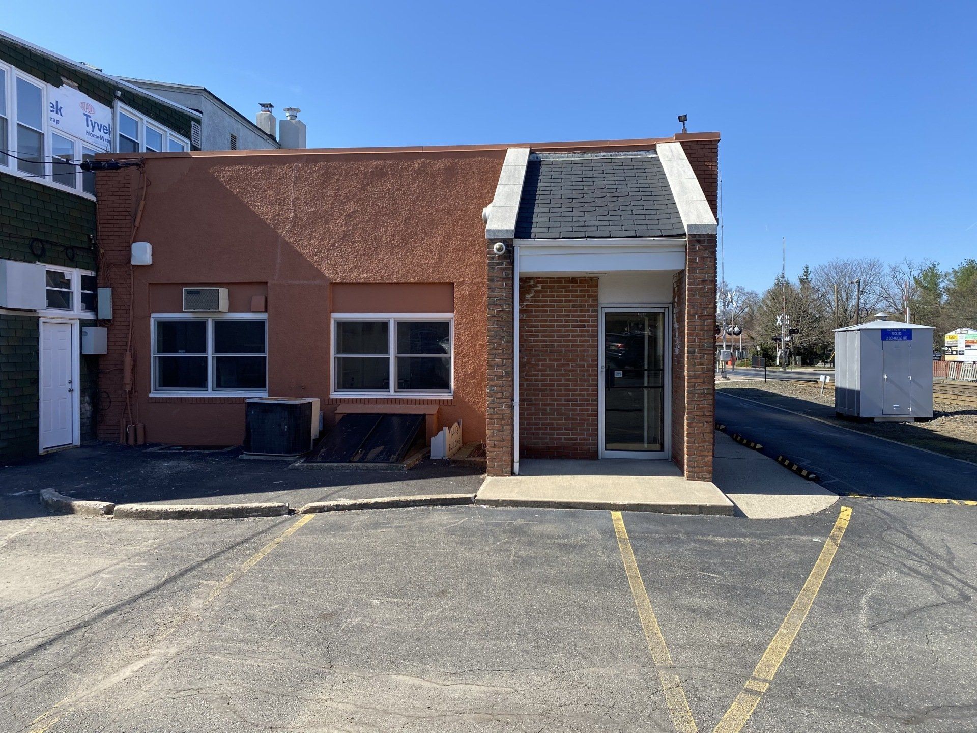 Brown brick building with glass door and windows, in parking lot on a sunny day.