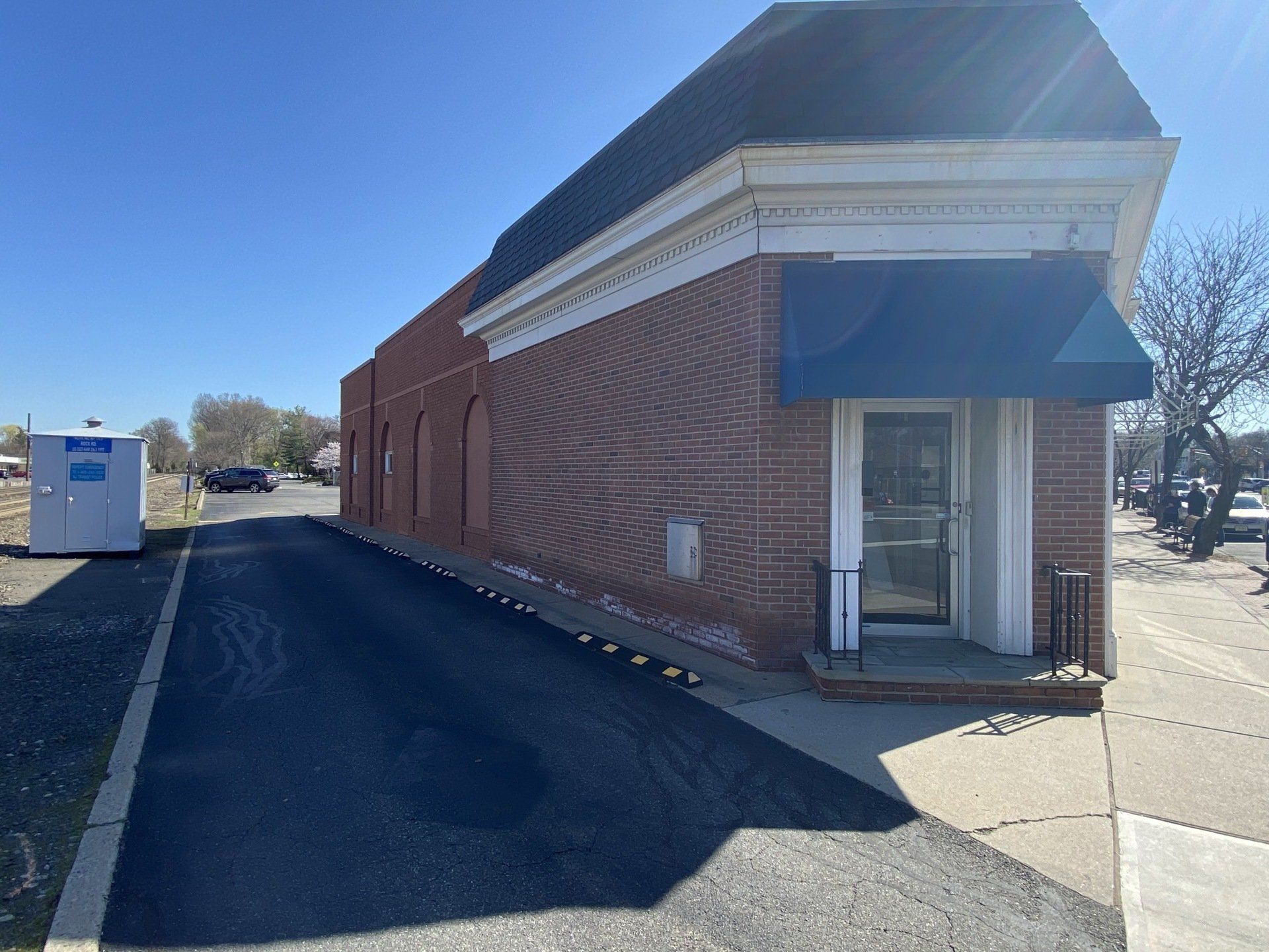 Brick building with a blue awning over the entrance. A paved path leads toward the entrance.