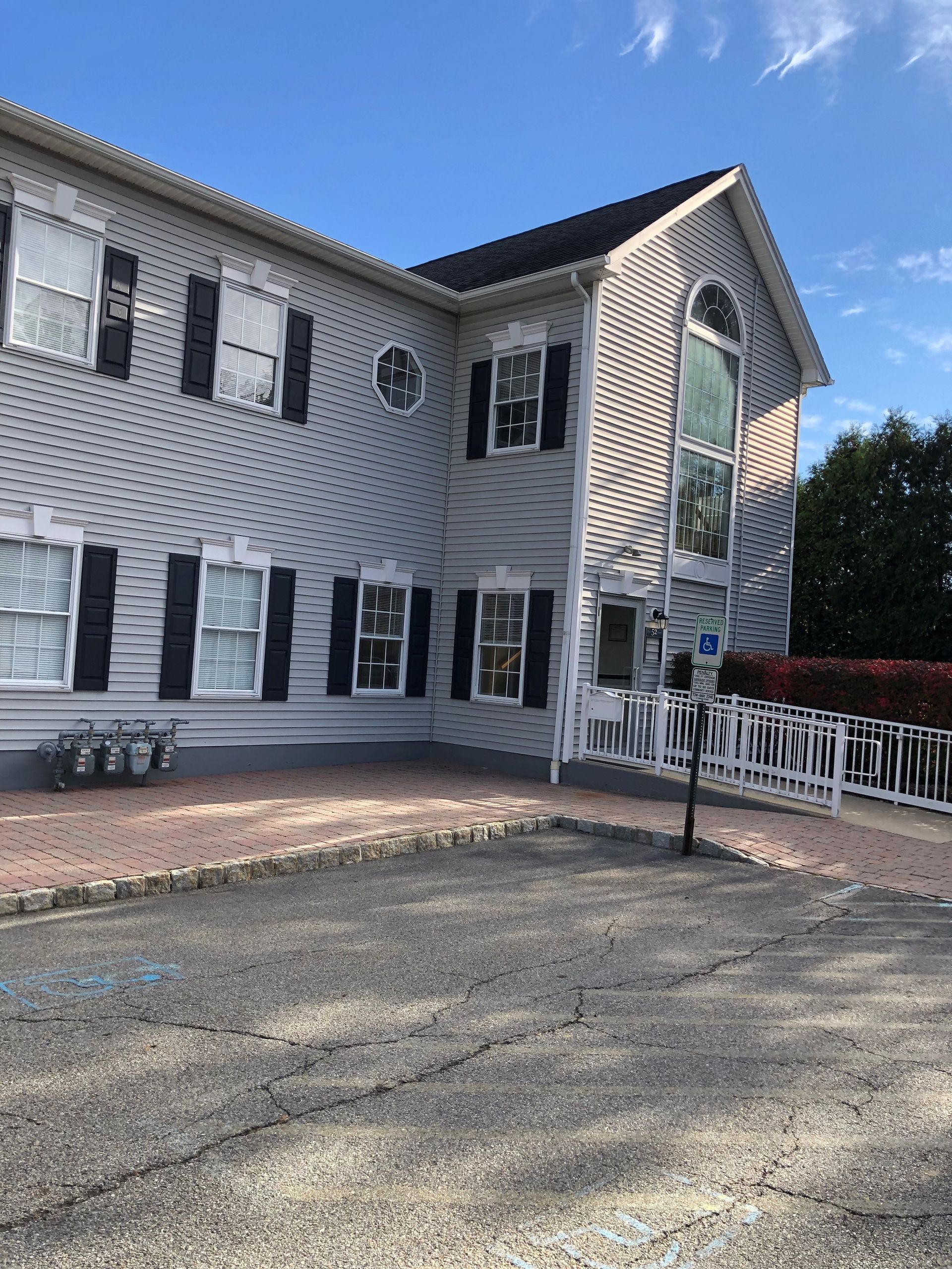 Two-story light gray building with black shutters and a wheelchair ramp. Blue sky background.