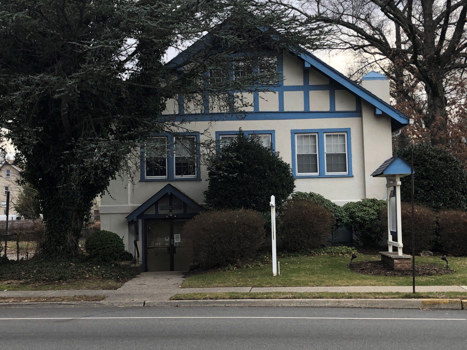 Two-story building with blue trim, bushes, and a small sign in front of the building.