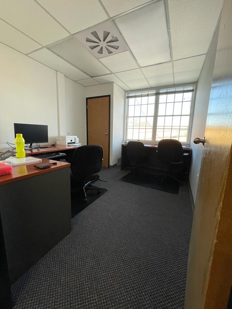 Office with desks, chairs, window, and door; neutral colors.