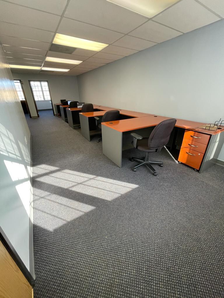 Office space with several desks, chairs, and file cabinets. Gray carpet and pale blue walls.