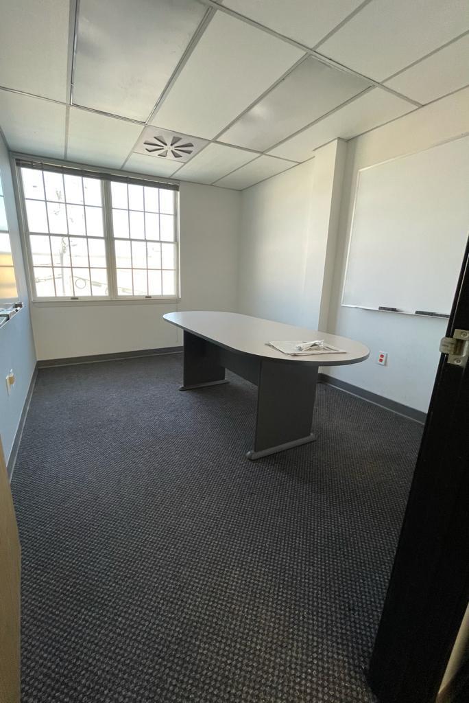 Empty conference room with a long oval table, window, whiteboard, and gray carpet.