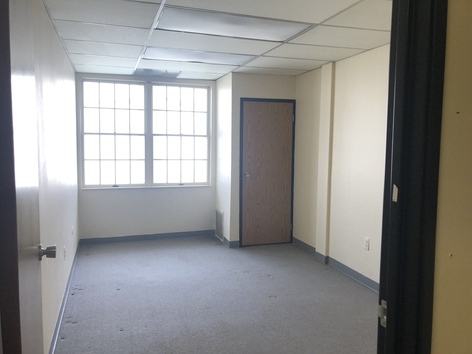 Empty room with window, door, and gray carpet. Beige walls, white ceiling.