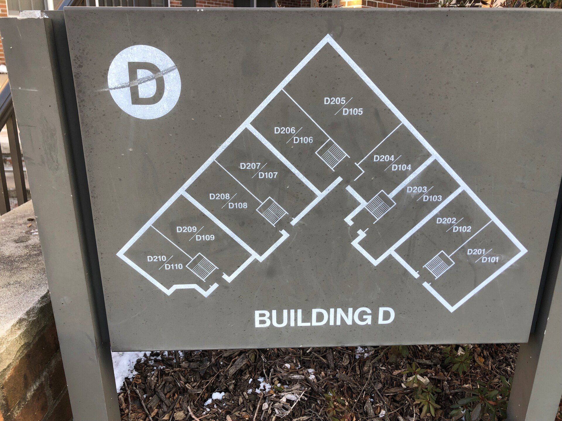 Sign with white layout of Building D apartments, on gray background.