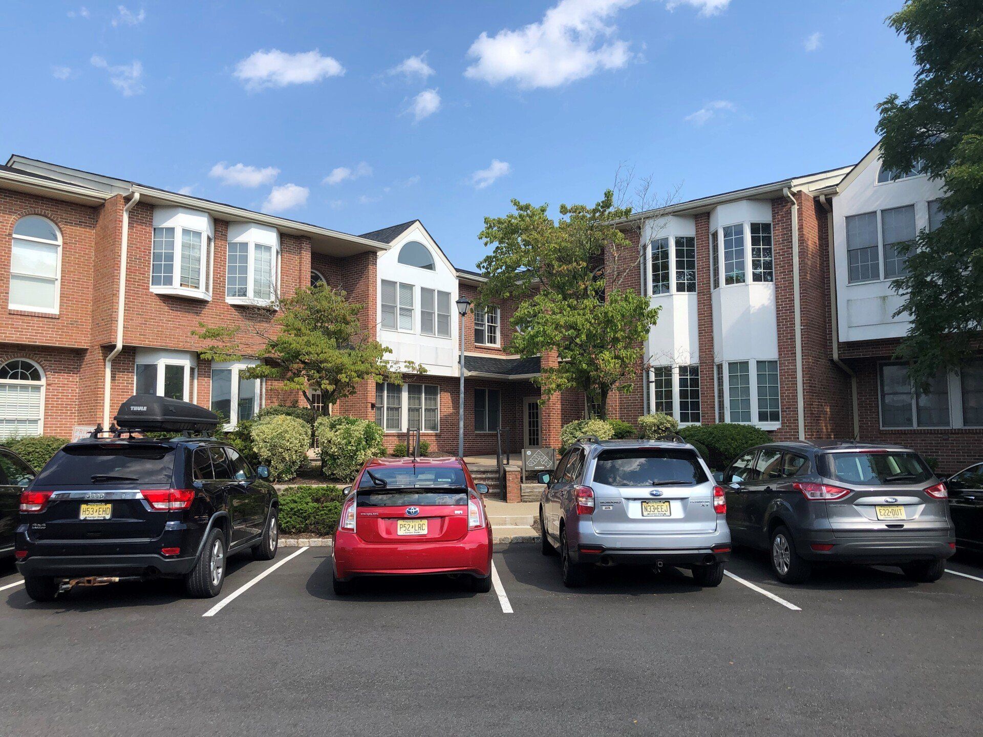 Cars parked in front of a brick apartment building with white trim under a blue sky.