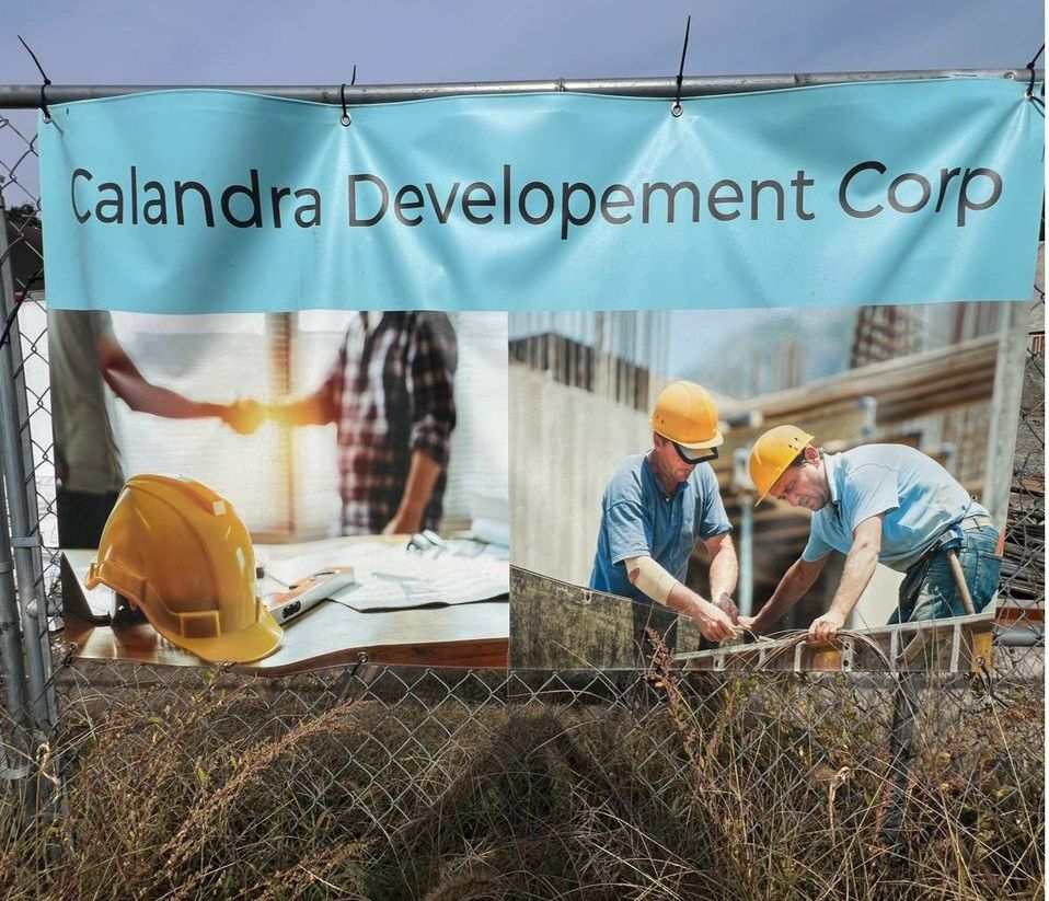 Sign for Calandra Development Corp with construction workers and a handshake.