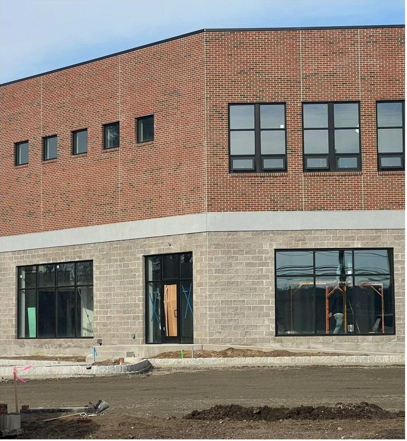 Building exterior under construction; red brick upper section, gray block lower section, large windows.