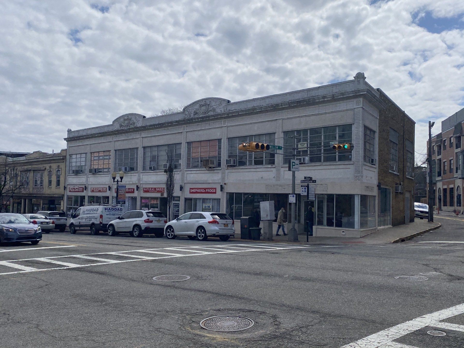 Two-story building at a street corner with shops on the ground floor. Cars parked along the street.