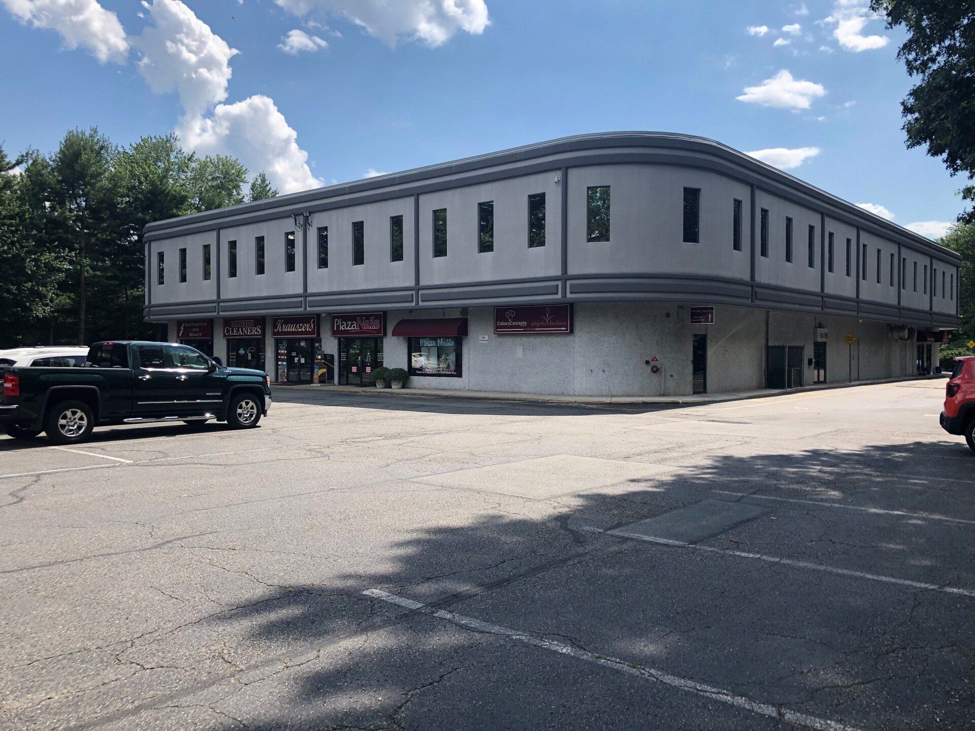 Gray commercial building with parking lot; a black truck and red SUV are parked.