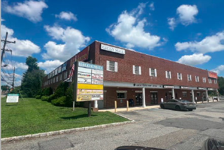 Two-story brick building with businesses and parking; a sunny day.