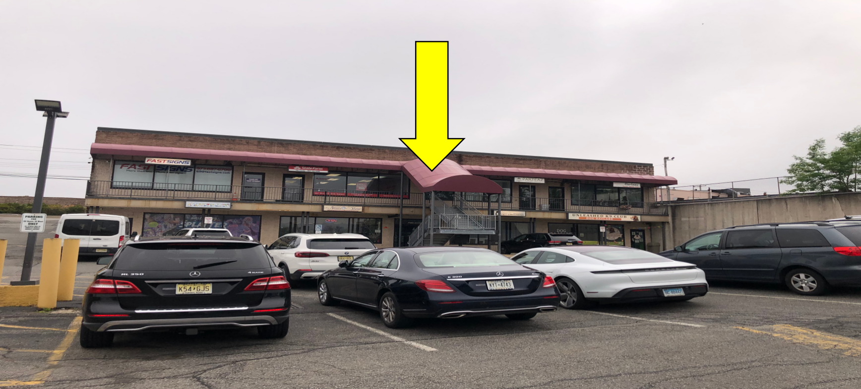 A yellow arrow points toward the entrance of a two-story commercial building with a parking lot in the foreground.