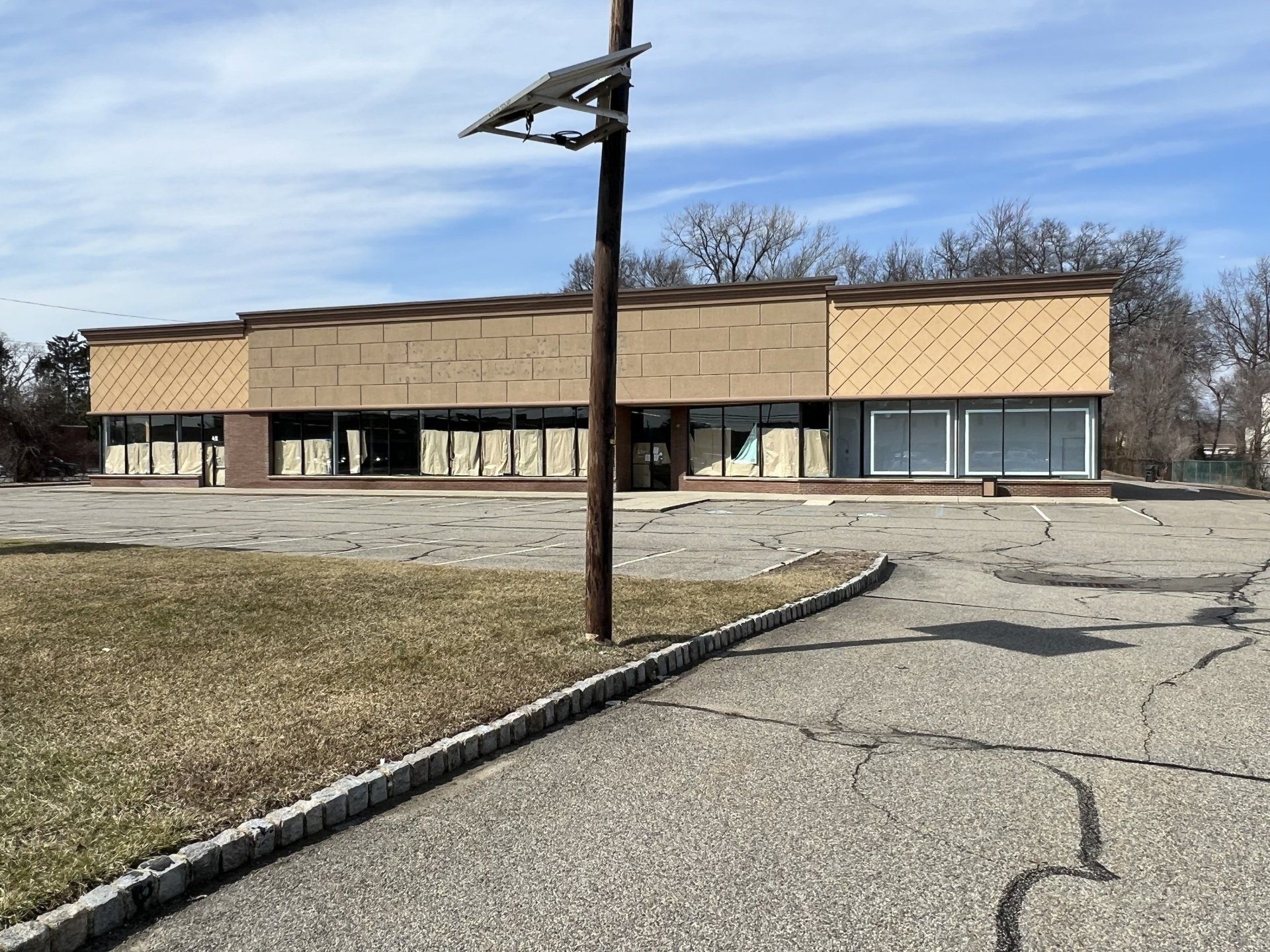 Vacant, run-down single-story commercial building with broken windows, cracked pavement, and utility pole.