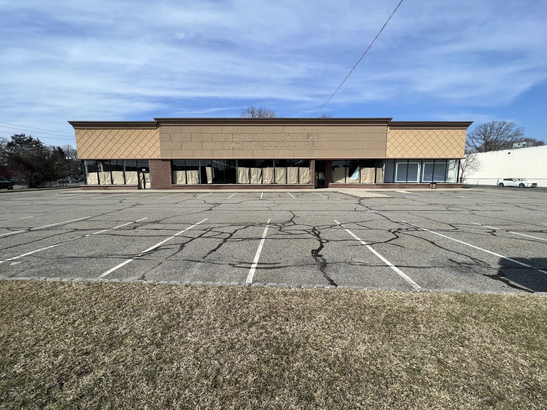 Exterior view of a vacant, single-story commercial building with a cracked parking lot and overcast sky.