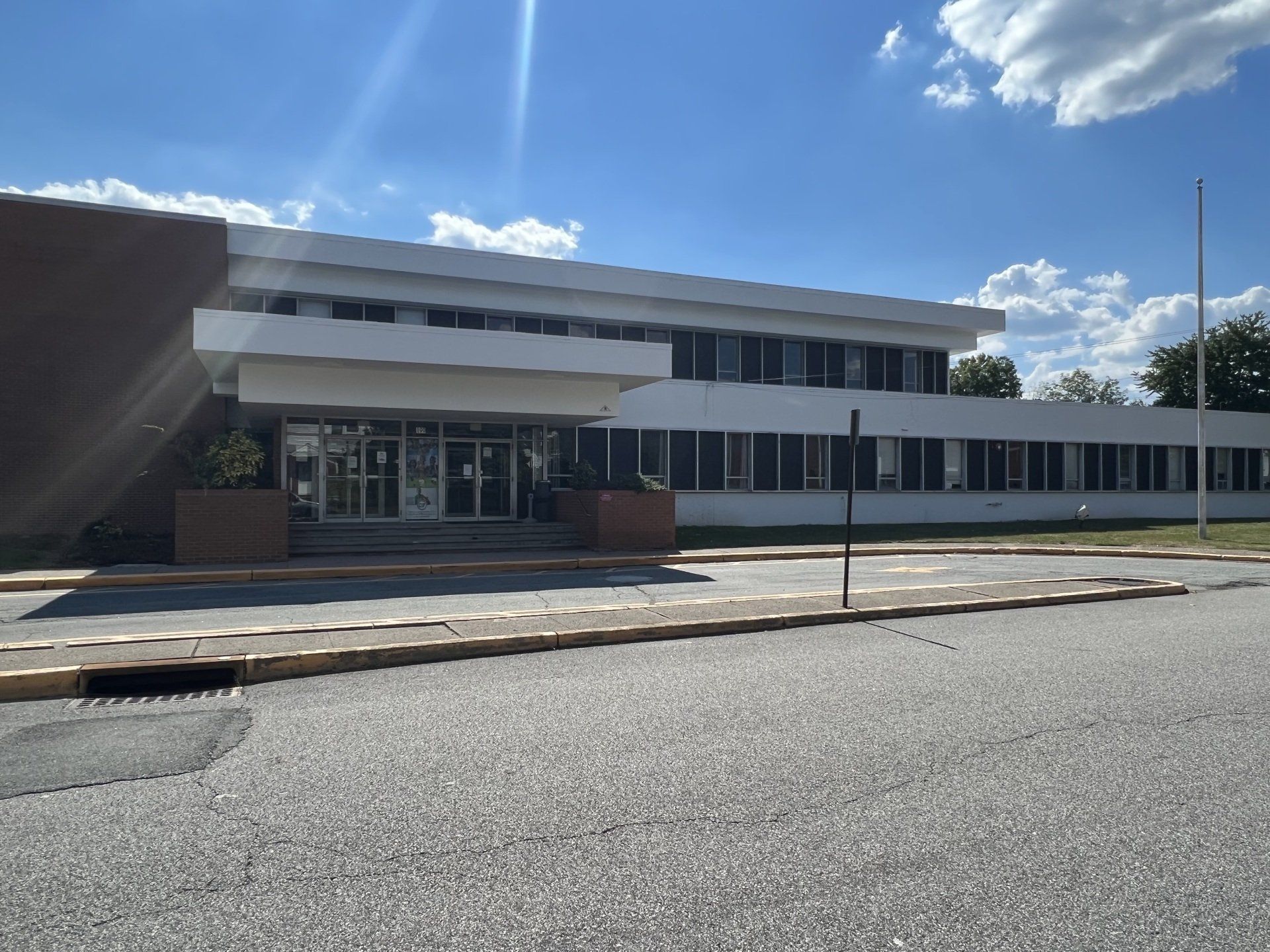 Two-story white building with a flat roof, large windows, and a small entrance overhang on a sunny day.