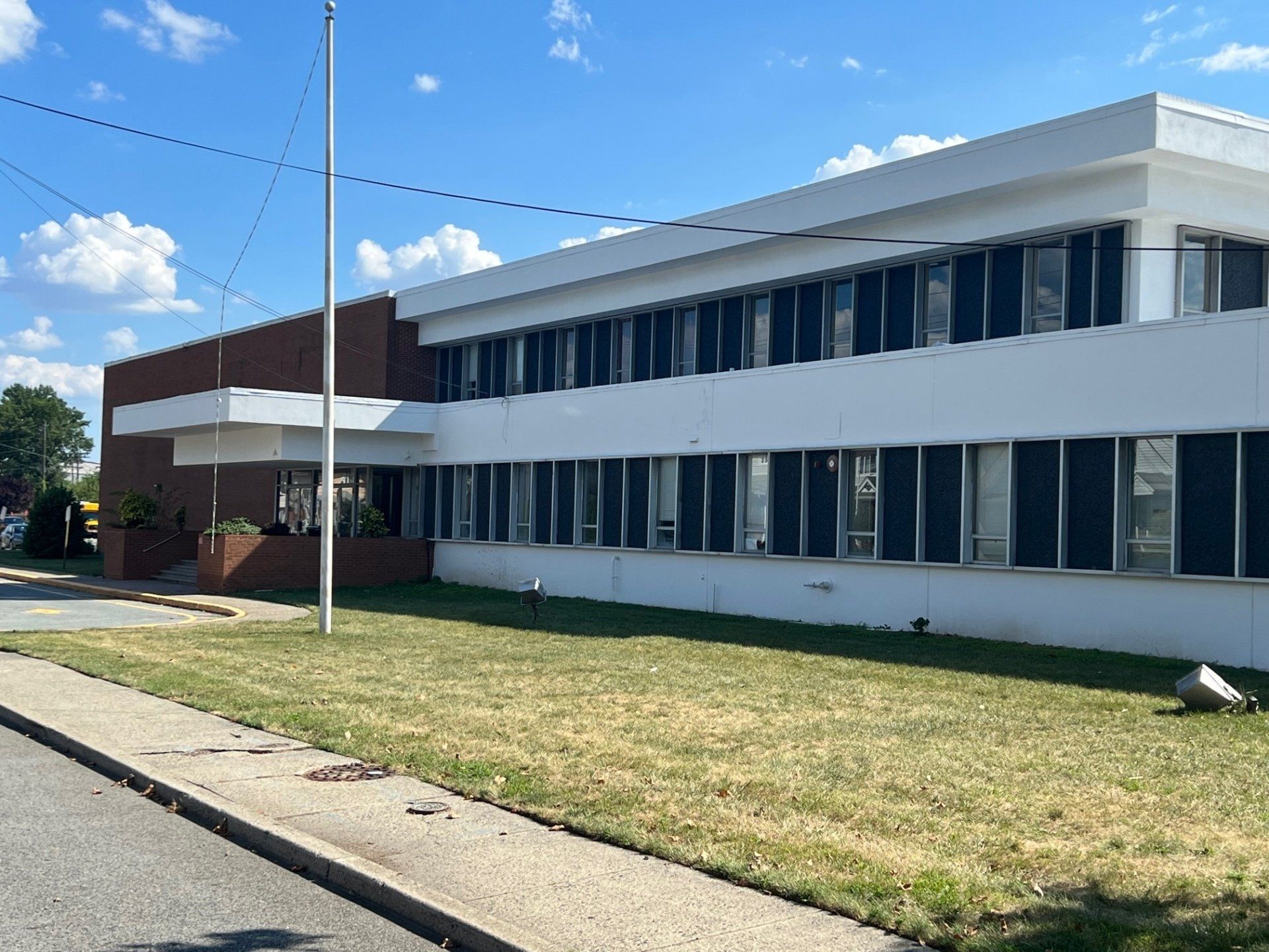 White office building with many windows, brick accents, and a flagpole on a sunny day.