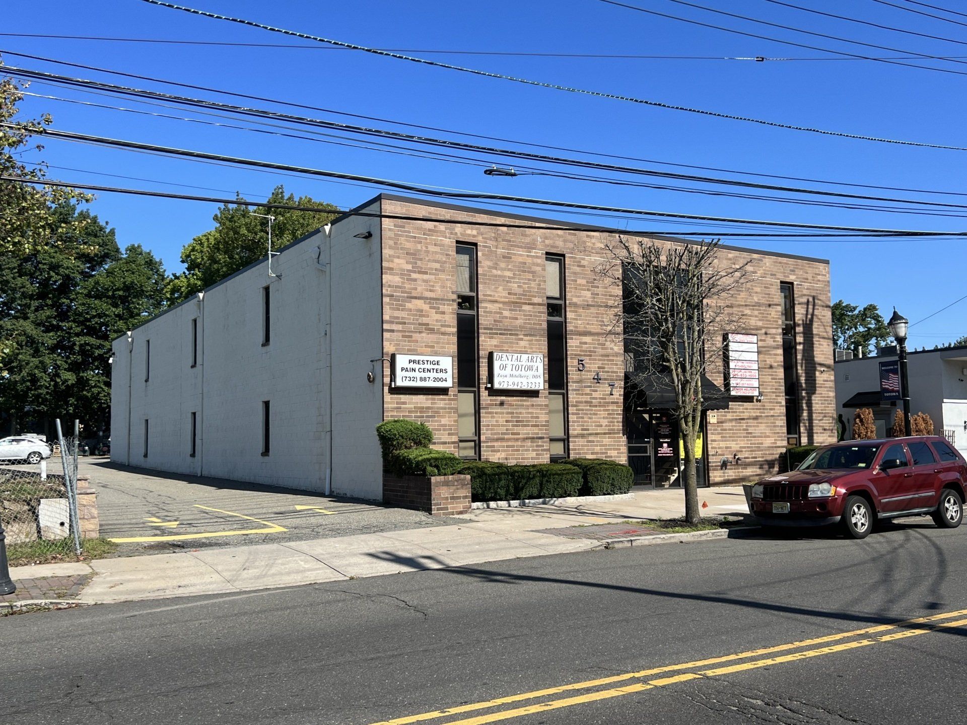Brick building with three signs, parked SUV, power lines, and blue sky.