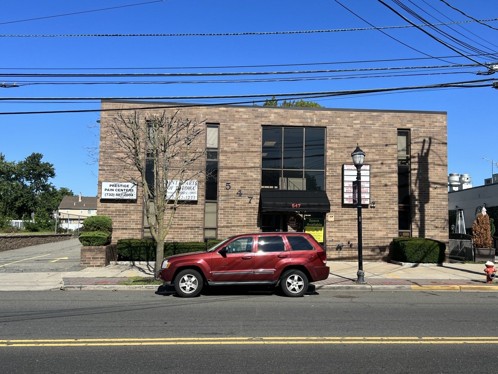 Red SUV parked in front of a brick building with windows and a black awning. Clear blue sky.