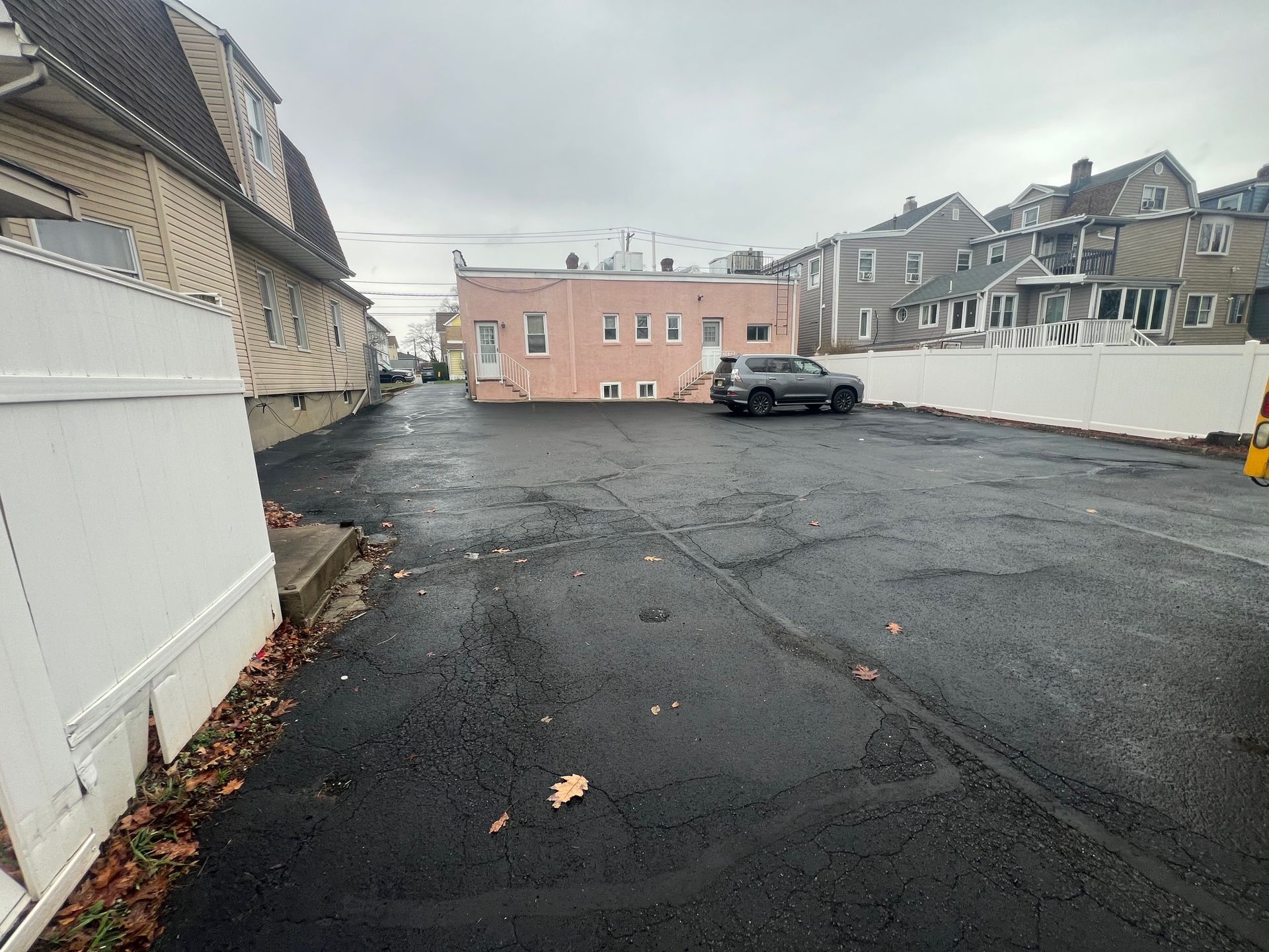 An asphalt parking lot area between residential buildings with a parked grey SUV in the background.