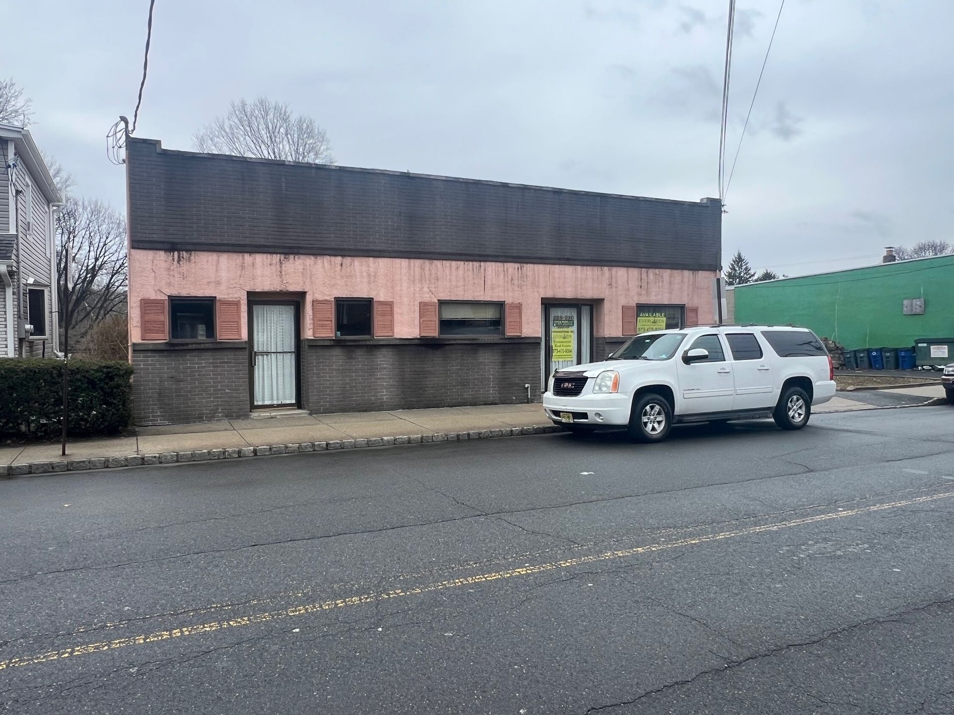 A single-story, pink commercial building with a dark facade, parked with a white SUV in front on an asphalt street.