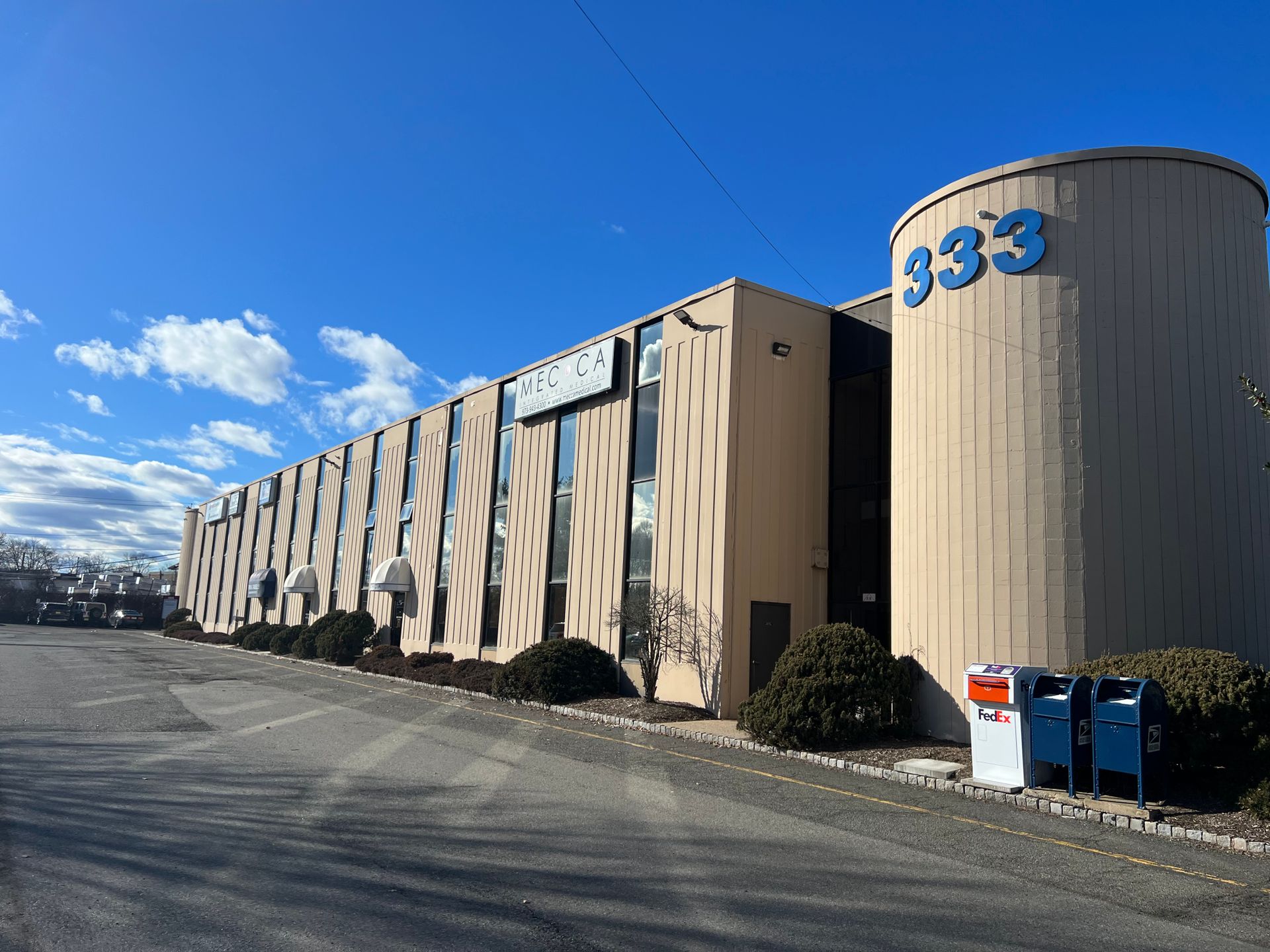 Building with address 333, tan and grey facade, blue sky, parking lot, mailboxes.