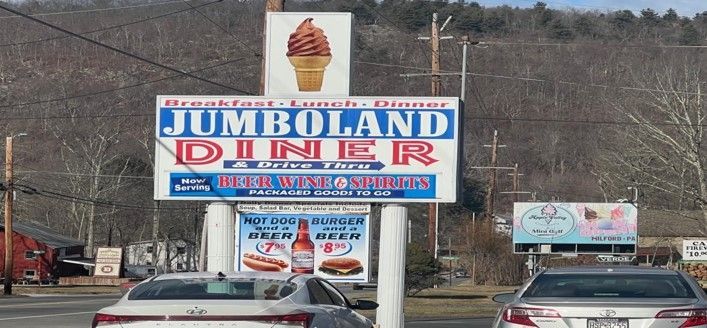 A sign for jumboland diner is above a parking lot with cars parked in front of it.