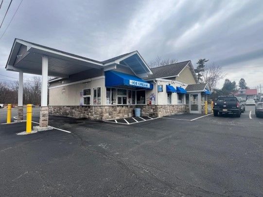 A white building with a blue awning and a parking lot in front of it.