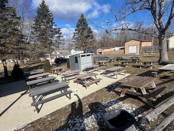 A row of picnic tables in a park with a shed in the background.