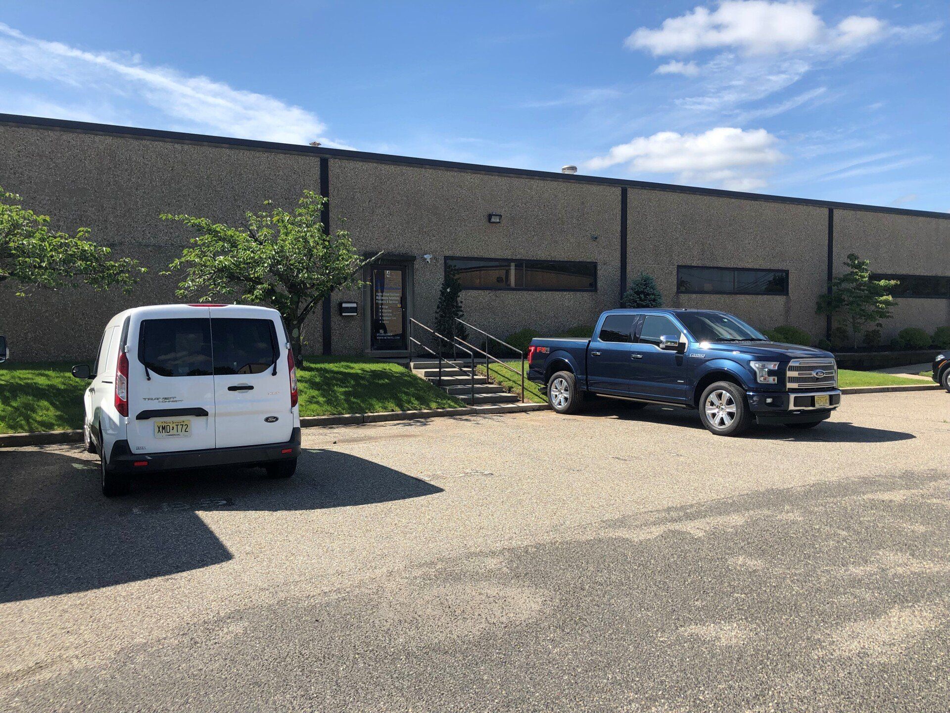 White van and blue truck parked outside a brick building under a blue sky.
