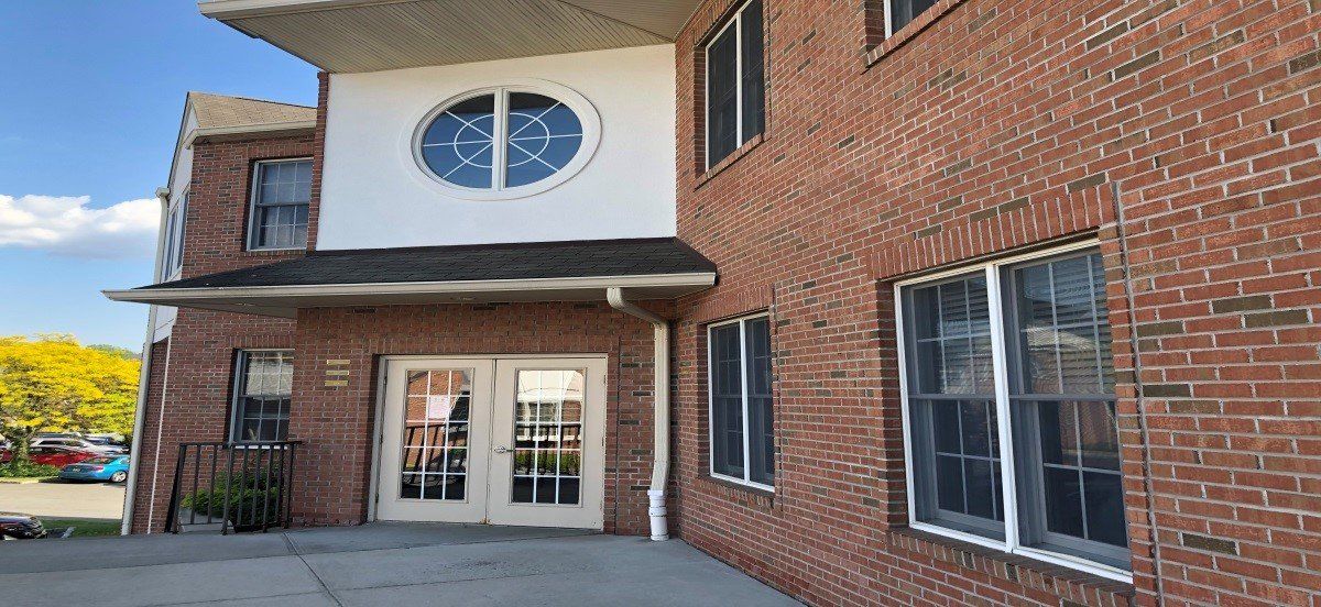 Brick building with white trim, arched window with an anchor design, and double doors.