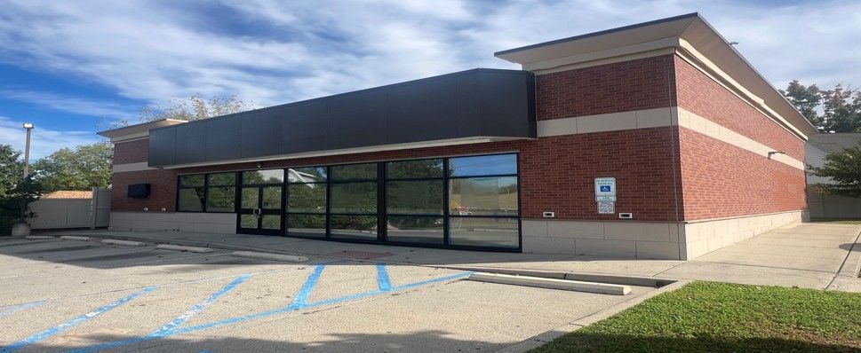 Single-story brick storefront with large windows, parking lot, and blue-striped accessible parking spaces