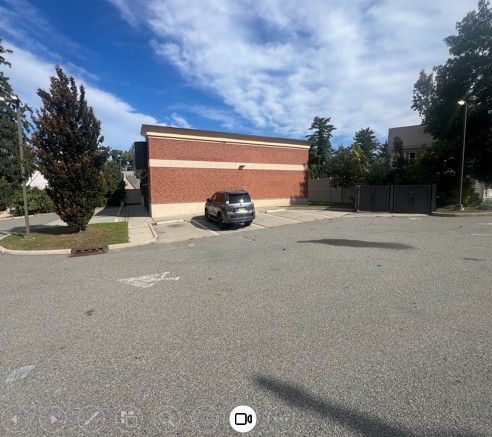 Empty parking lot with a black car in front of a red brick building under a blue sky