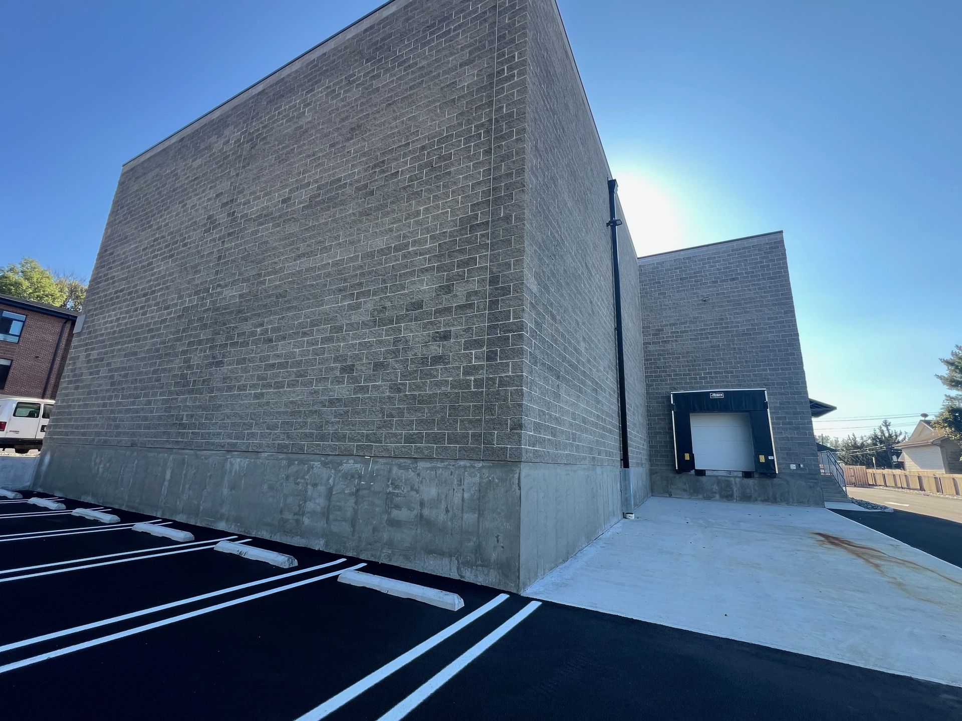 Gray brick building with loading dock next to a parking lot under a bright blue sky.