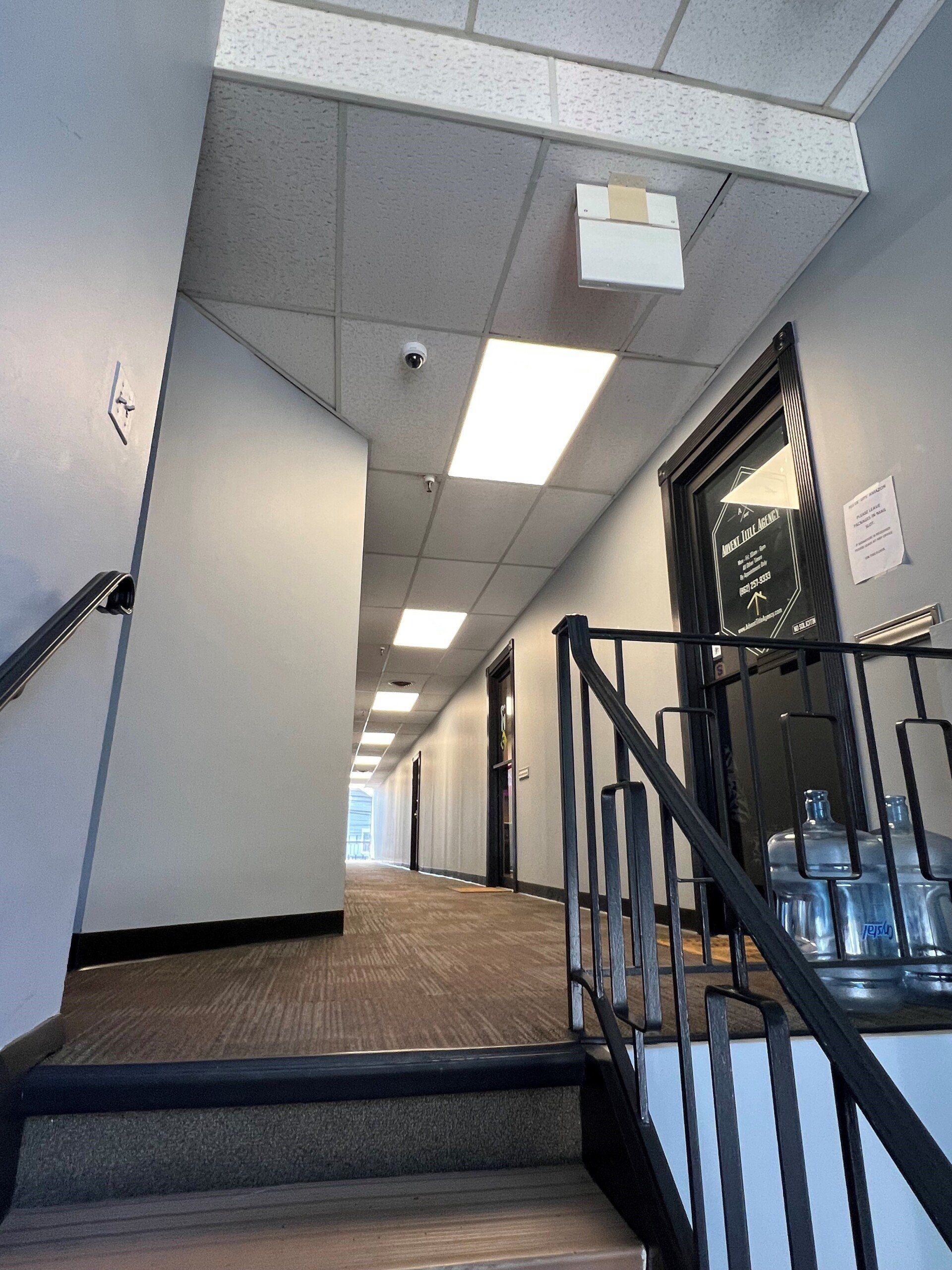 Interior office hallway with doors, stairs with railing, and fluorescent ceiling lights.