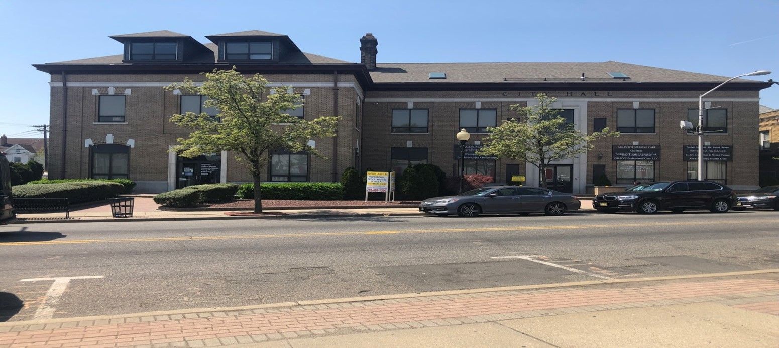 Brick building with multiple windows, parked cars on street.