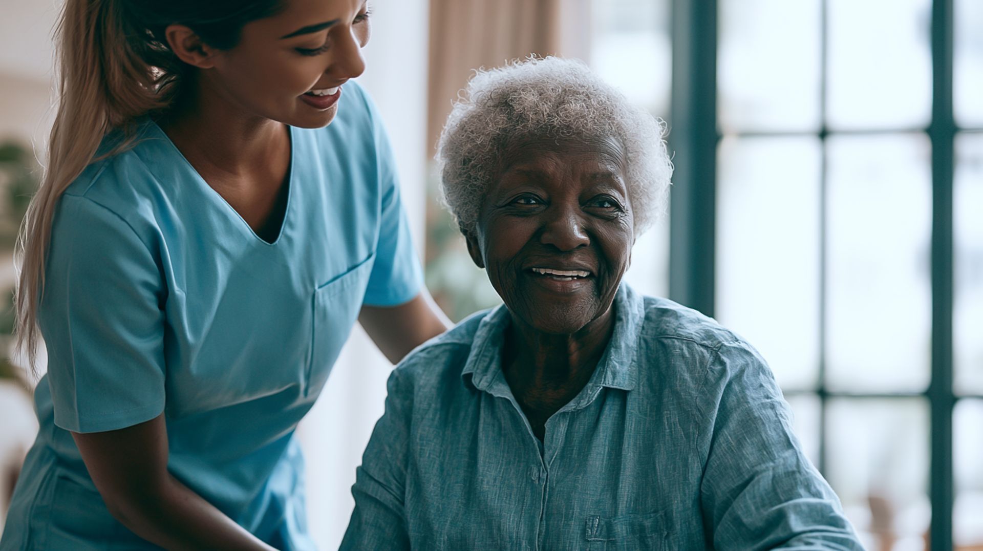 Woman gently supports an older woman seated at a table with a glass, in a bright home kitchen.