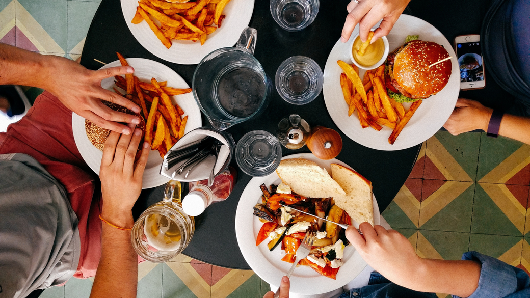 People eating lunch at a table with fries, burgers, and other dishes.