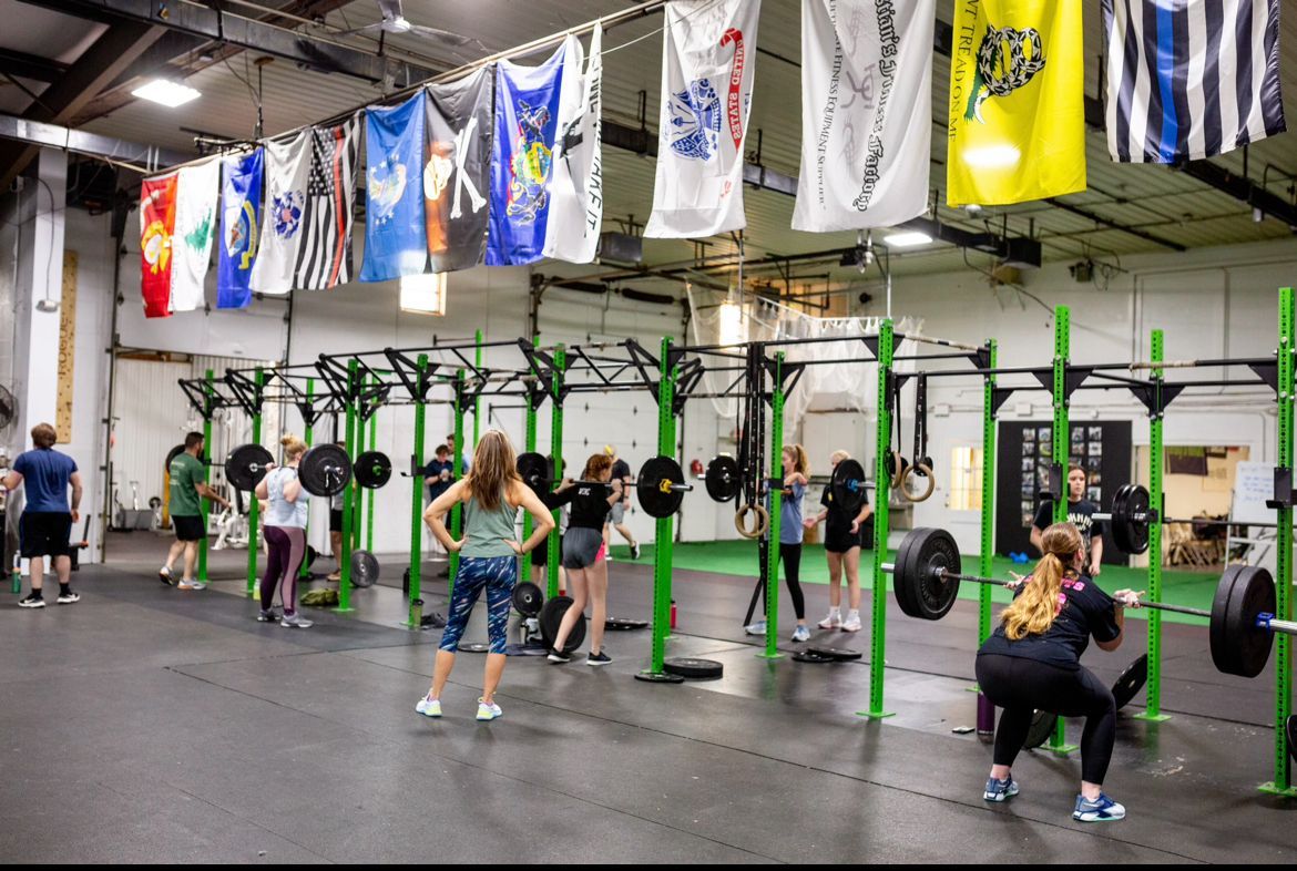 A group of people are doing squats in a gym with flags hanging from the ceiling.