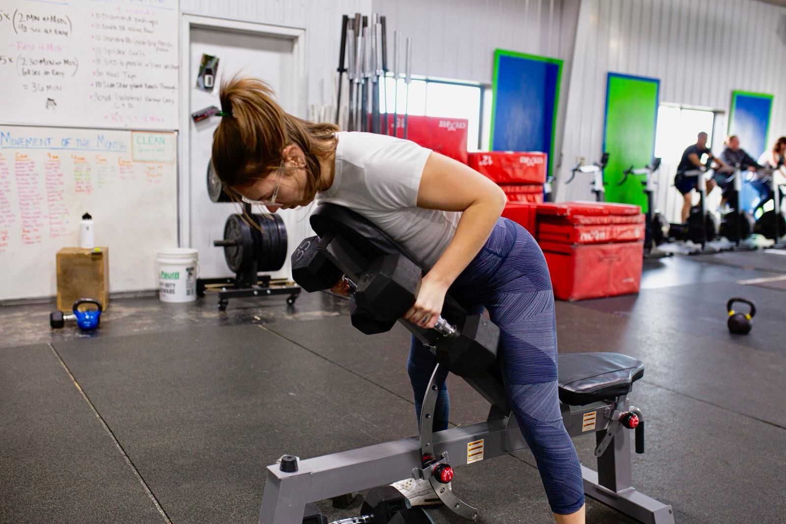 A woman is lifting a dumbbell on a bench in a gym.
