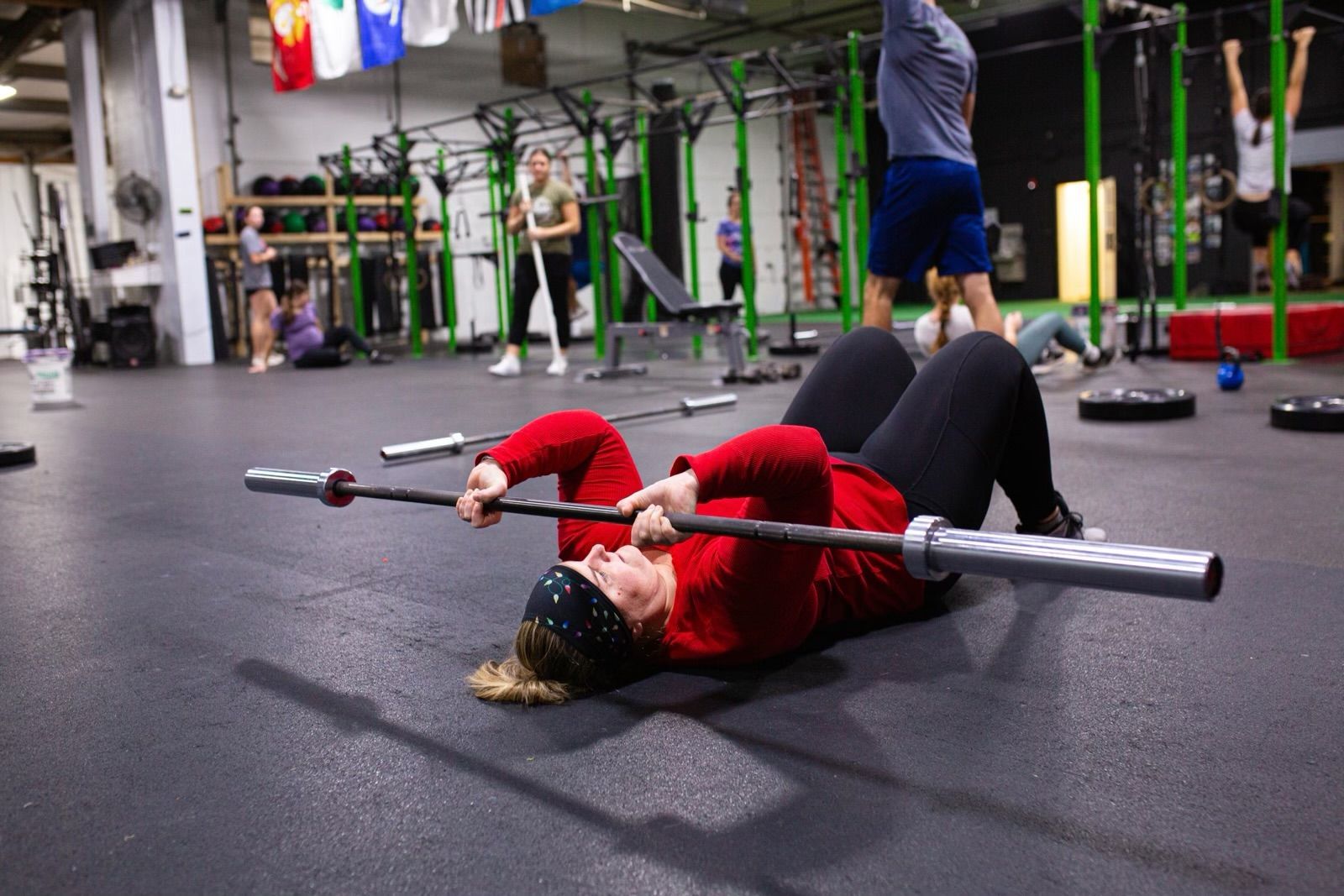 A woman is laying on the floor holding a barbell in a gym.