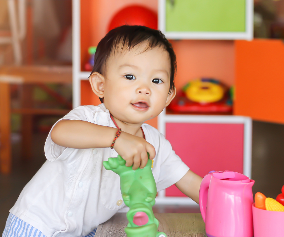 A baby is playing with a green toy frog