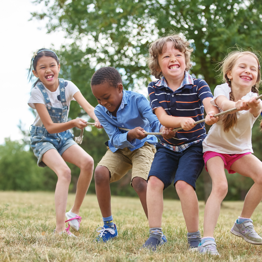 A group of children are pulling a rope in a field.