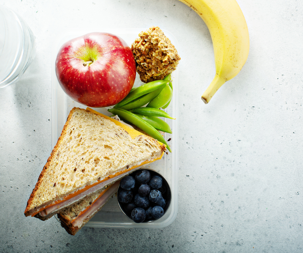 A lunch box with a sandwich , apple , banana , green beans and blueberries.