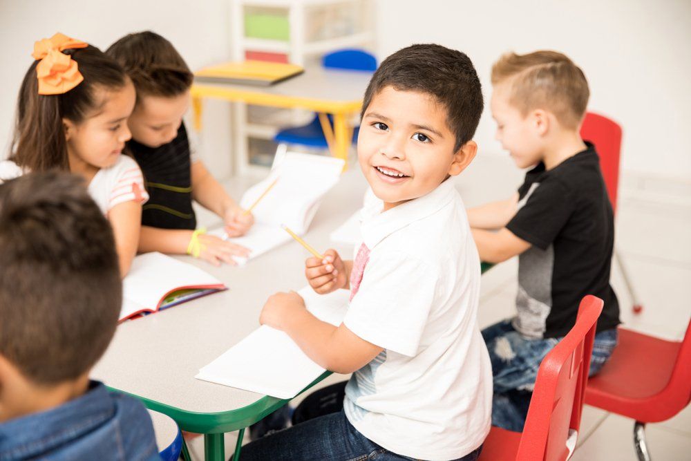 A group of children are sitting at a table in a classroom.