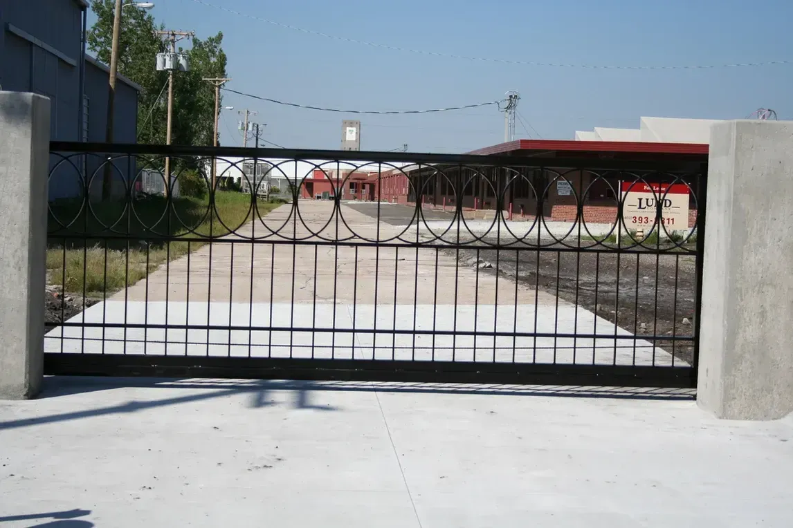 a sliding gate is open to a driveway with a building in the background