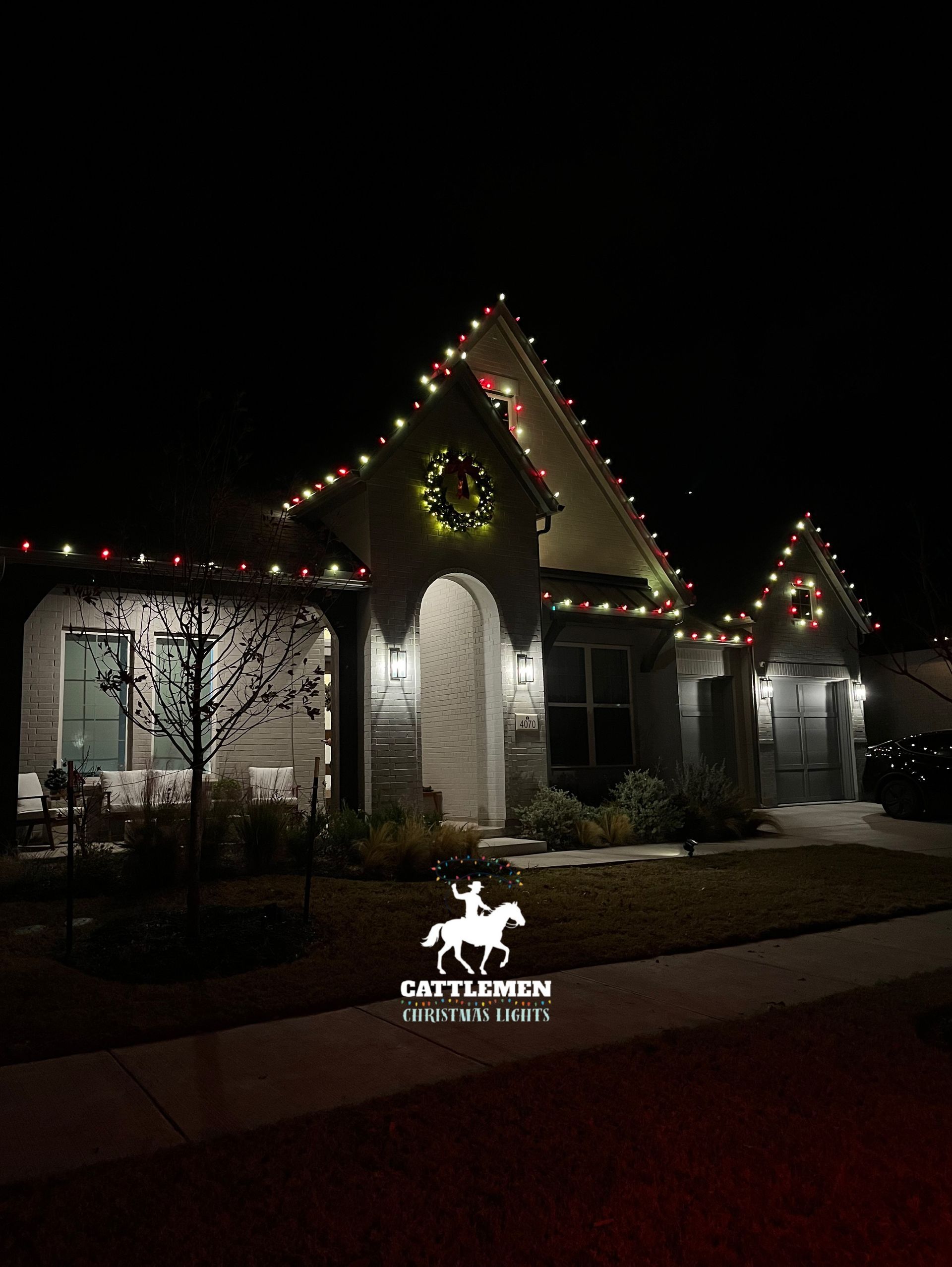 Lit stone building decorated with colorful holiday lights at night, with a small sign in front.