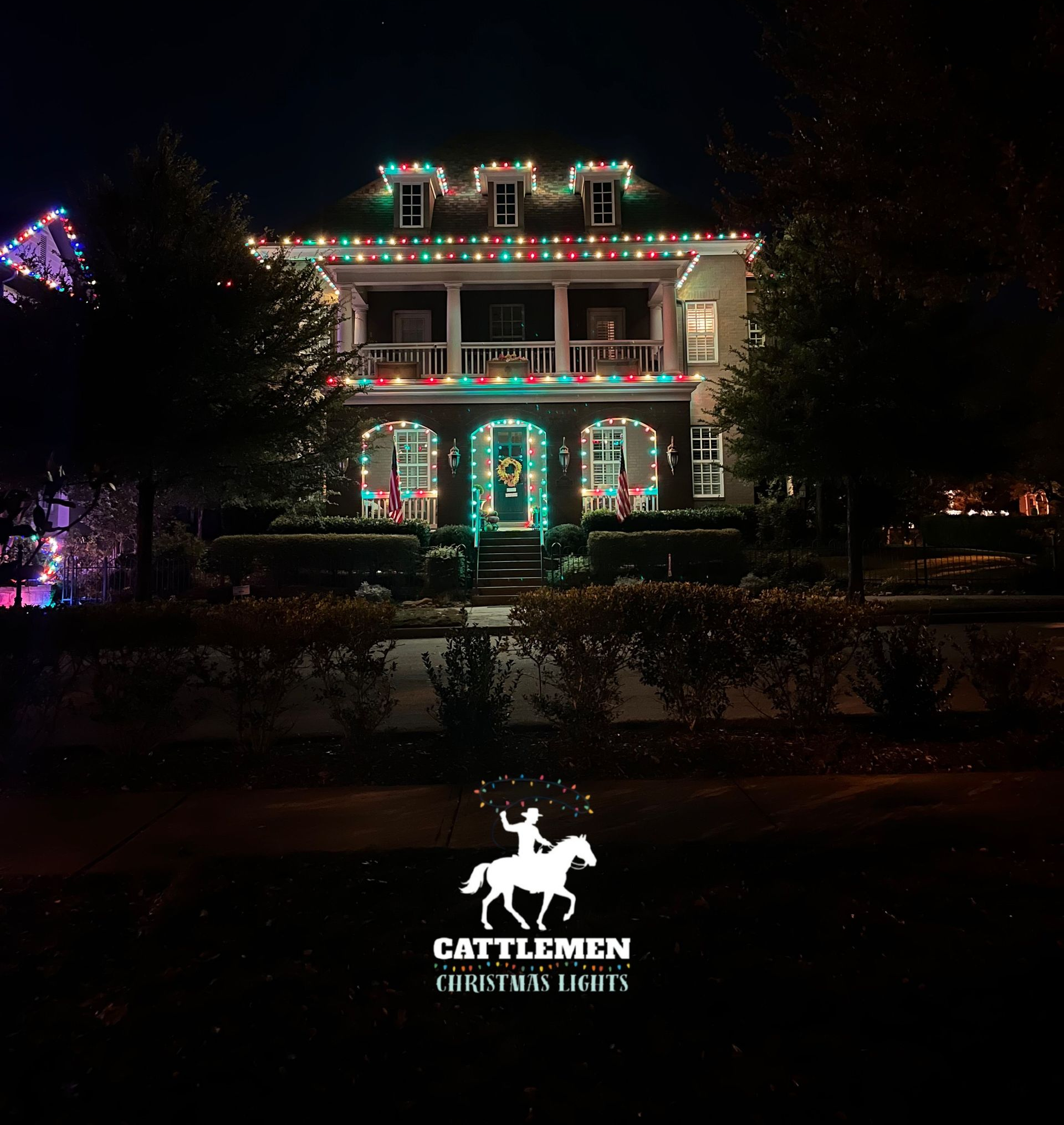 House outlined in colorful Christmas lights at night, with a Cattlemen Steakhouse sign in front.