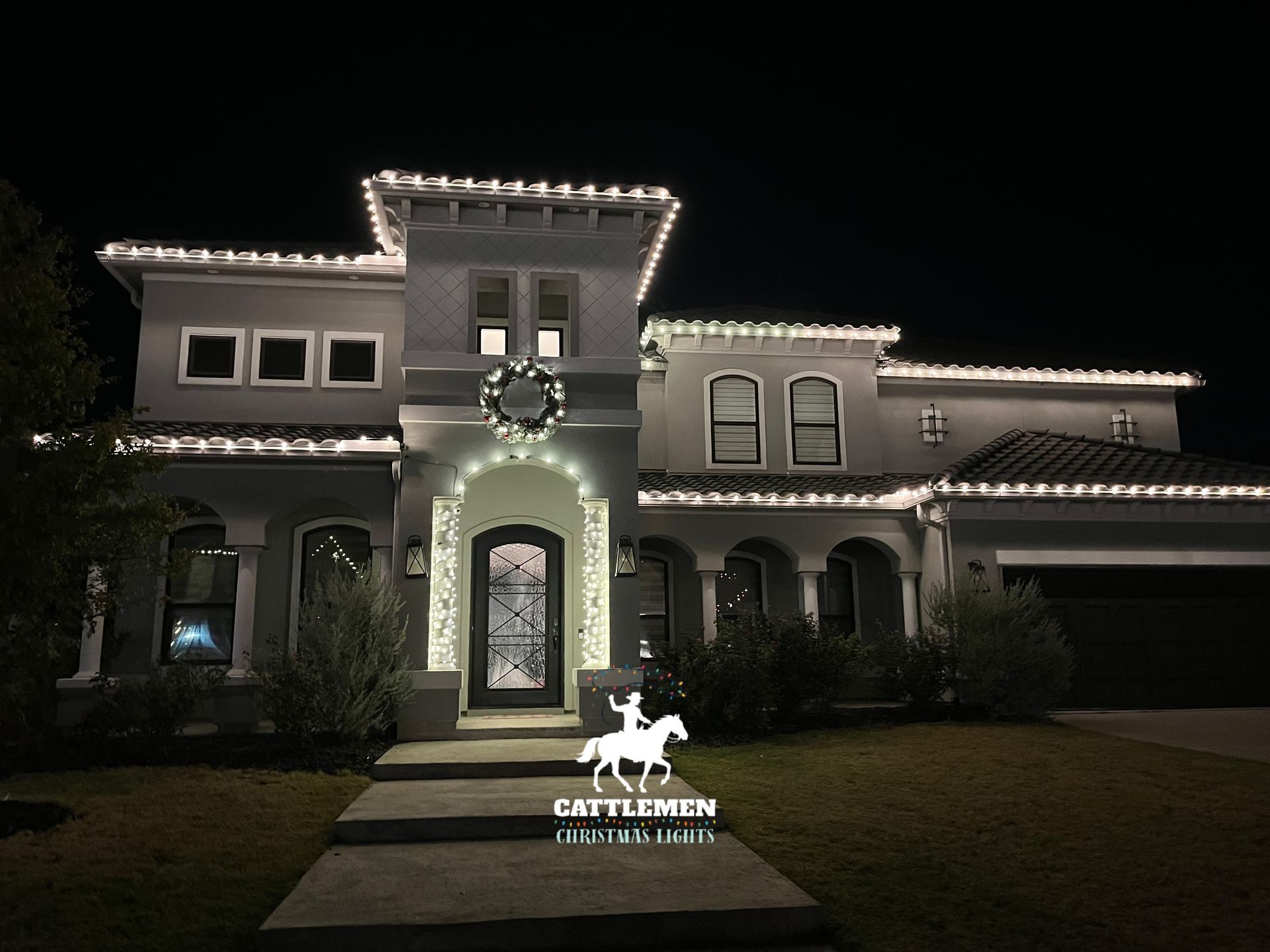 Illuminated two-story house at night with white lights outlining the roof and windows.