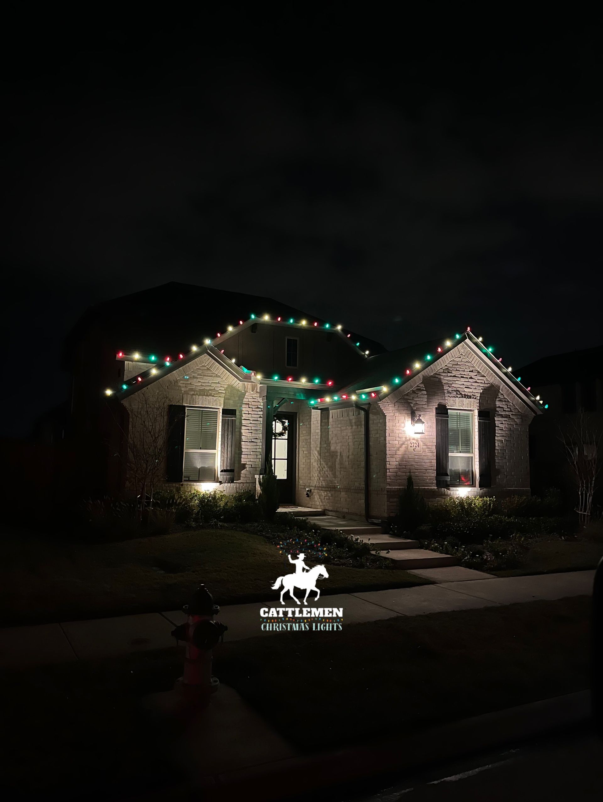 Small house at night with colorful holiday lights along the roof and front walkway.