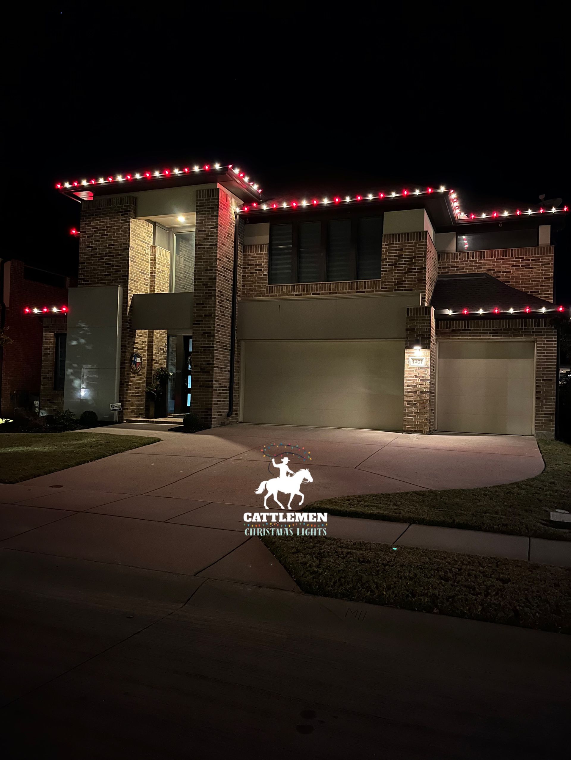 Two-story house at night with red roof lights and a lit garage in front